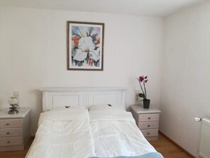 Et soveværelse med en seng, et natbord, en blomsteropsætning i ramme og en potteplante.