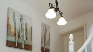 A staircase with white balusters, two wall-mounted paintings, and a hanging light fixture.