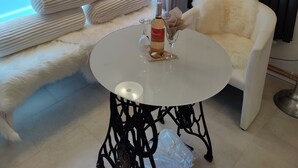 Een moderne kamer met een witte bank, een ronde tafel met een fles en glas, en een raam met jaloezieën.