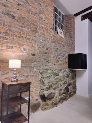 Ein Zimmer mit Backsteinwand, einem Holztisch mit Lampe und einem Wand-Fernseher.