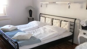 Un dormitori amb un llit doble, una taula de nit, una làmpada, un radiador, una taula rodona i una cadira blanca.