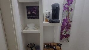 Un bany compacte amb cafetera, paperera i prestatgeries amb productes de tocador.