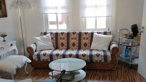 Una habitació amb un sofà estampat, una taula rodona, un llit i una làmpada de peu.