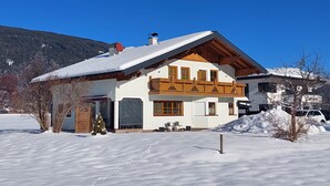 Eine zweistöckige Chalet mit geneigtem Dach, Holzbalkon und verschneiter Landschaft.