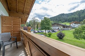 A wooden balcony with a view of a parking area and buildings in a mountainous area.