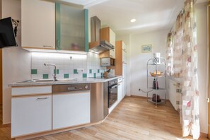 A compact kitchen with a dishwasher, oven, and a coffee machine on a shelf.