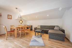 A modern living room with a wooden dining table, chairs, a grey sofa, and a small coffee table.