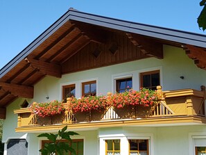 A building with a balcony adorned with flowers, wooden beams, and a green facade.