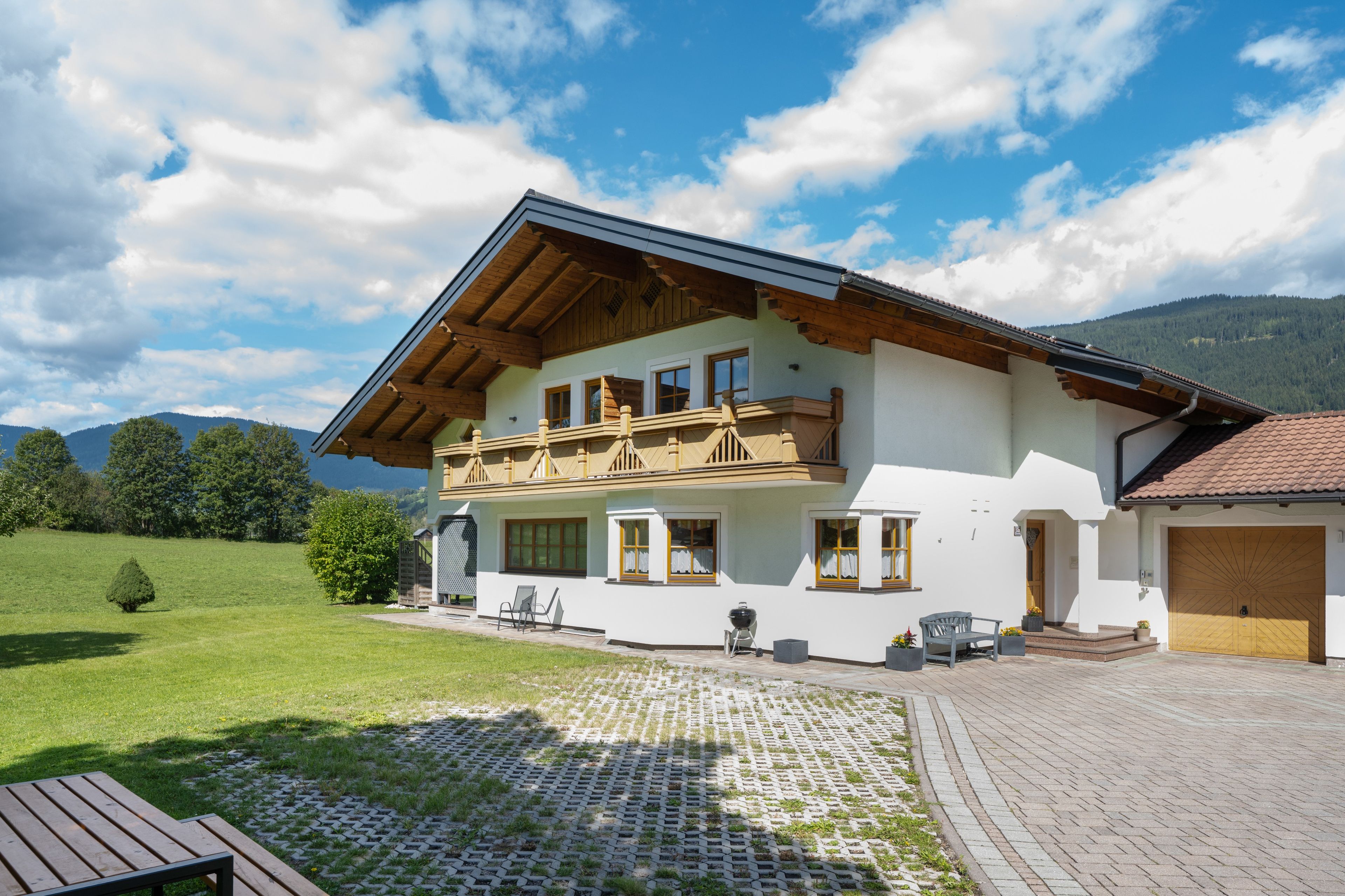 A two-story house with a balcony, a paved driveway, and a view of the mountains.