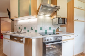A compact kitchen with a built-in oven, a microwave, and a stainless steel range hood.