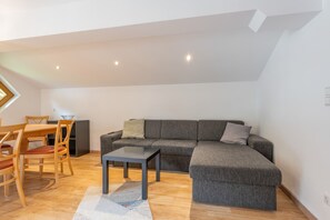 A modern living room with a sectional sofa, a dining table with chairs, and a small table.