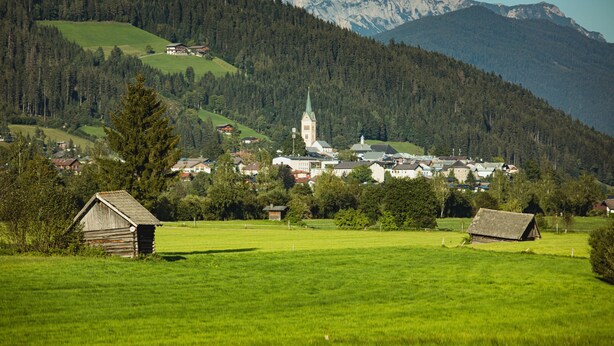 Ein ländliches Dorf mit einer Kirche, einem kleinen Holzhaus und einem Berg im Hintergrund.