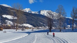 Schneebedeckte Landschaft mit blauem Himmel, einigen Skifahrern und einem Bergkamm im Hintergrund.