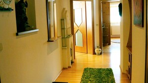 Un couloir avec un plancher en bois, un tapis vert, une zone carrelée et un miroir au mur.