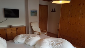 Une chambre à coucher comprenant un lit, une armoire en bois, une chaise, un téléviseur et un tableau accroché au mur.