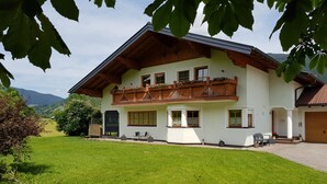 Une maison à deux étages avec un balcon, une porte d’entrée et une pelouse bien entretenue.