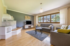 A modern living room with a flat-screen TV, grey sofa, and a dining area with a white cabinet and a wooden table.