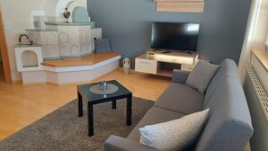 Un salon avec un canapé gris, une table basse noire, un téléviseur posé sur un meuble en bois et une cheminée blanche.