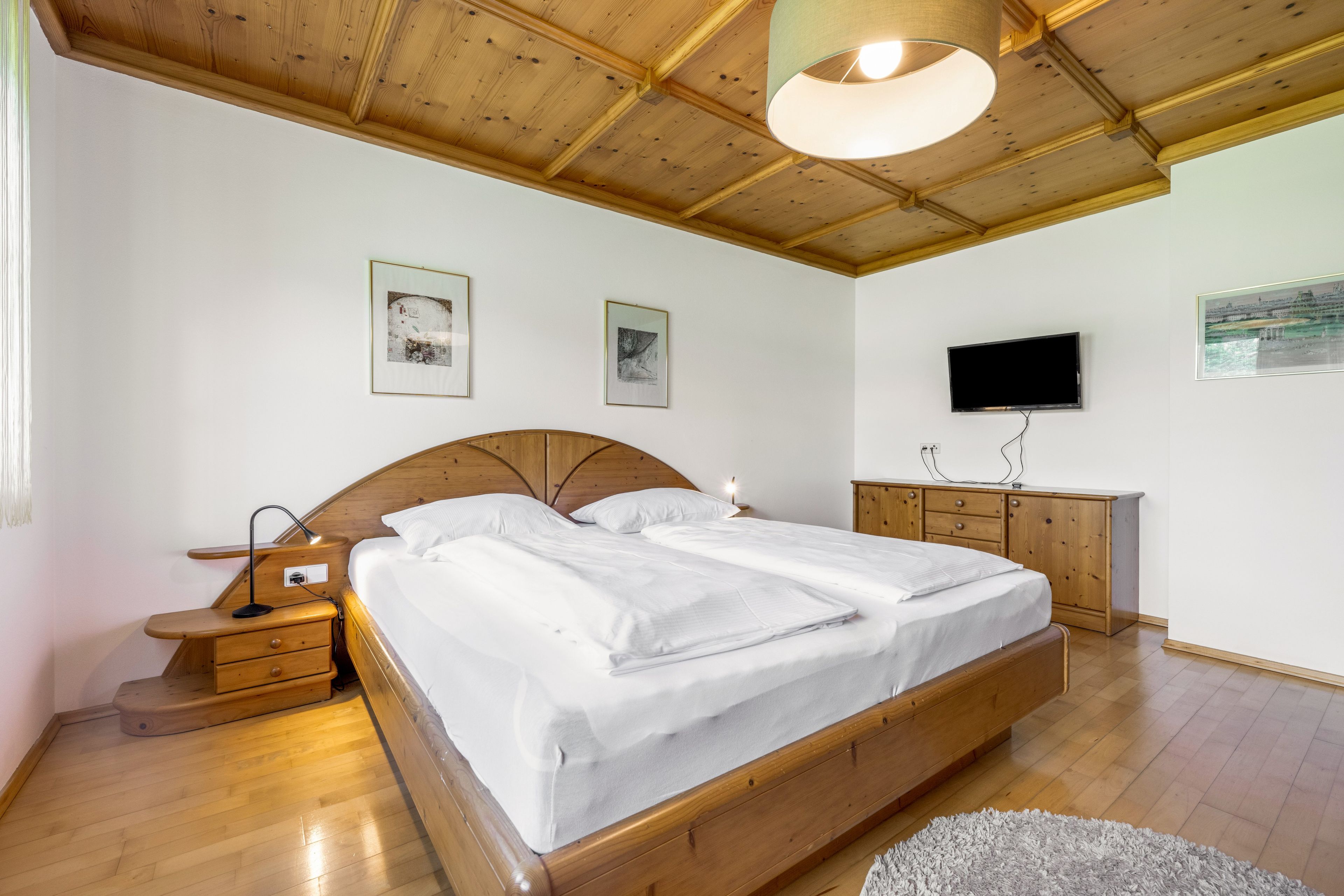 Un dormitorio con cama de madera, mesitas de noche, televisor de pantalla plana y obras de arte en las paredes.