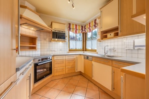 A kitchen with wooden cabinets, a built-in oven, a dishwasher, and a window with curtains.