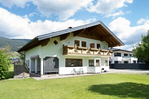 A two-story chalet with a balcony, a covered patio, and a view of the surrounding landscape.