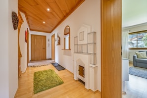 A hallway with wooden flooring, a green rug, a wooden door, and a fireplace with a white mantel.