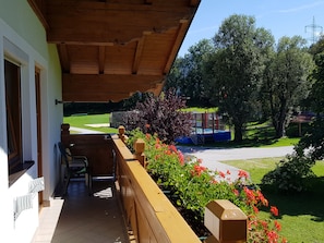 A wooden balcony with a view of a playground and green lawn.