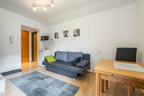 A modern living room with a grey sofa, a wooden dining table, and a patterned rug.