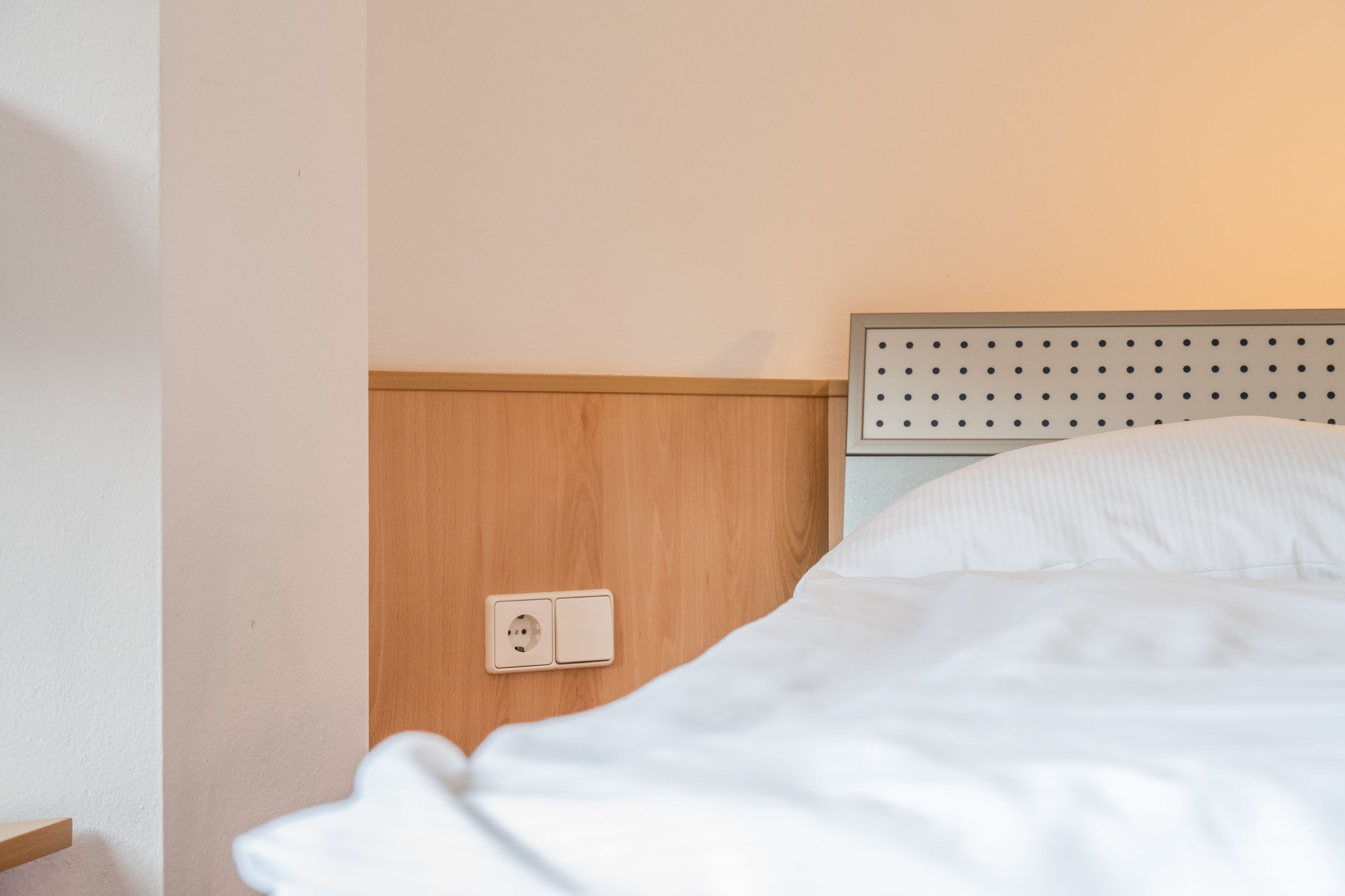 A hotel room with a wooden headboard, a white bed, and a wall socket.