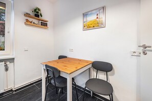 A small room with a wooden table, two chairs, a shelf with a plant, and a painting of a lighthouse.