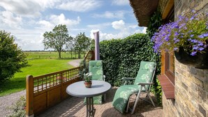 Een terras met een tafel en stoelen, een potplant en uitzicht op een groen veld.