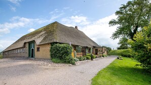 Een gebouw met rieten dak, een grindpad en een verzorgd gazon.