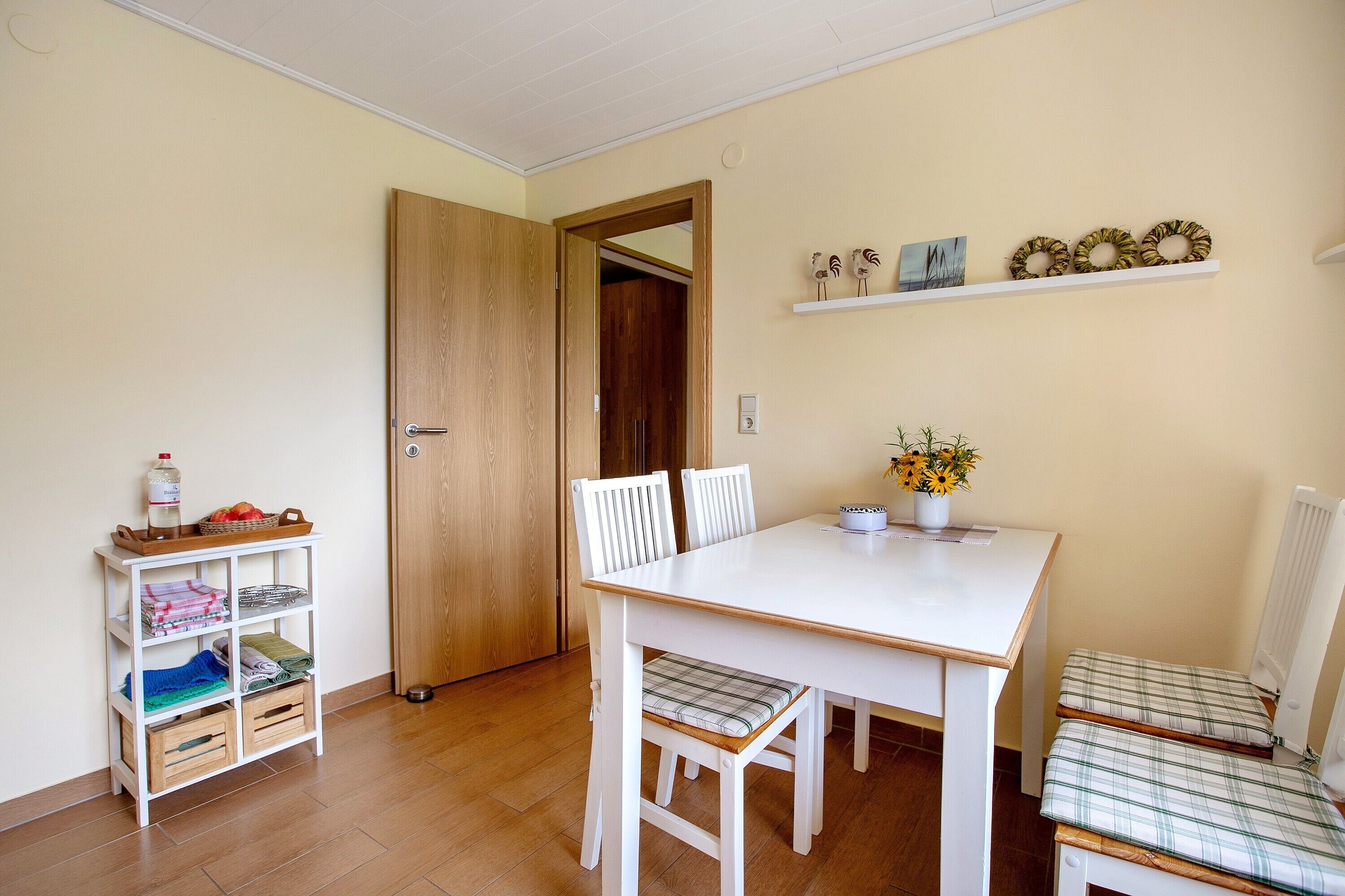 Un coin repas avec une table blanche, deux chaises, une petite étagère avec quelques objets et une porte en bois.