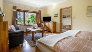 Een kamer met een bed, een slaapbank, een bureau, een televisie en een raam met uitzicht op groen.