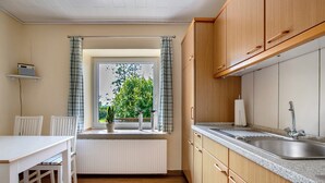 Een kleine keuken met raam, witte radiator, houten keukenkastjes en een spoelbak.