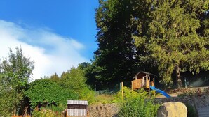 A rustic wooden structure with a checkered roof, surrounded by a garden with red flowers and a stone retaining wall.