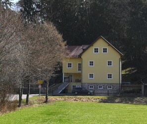 A two-story yellow building with a stone base, a staircase, and a car parked in front.