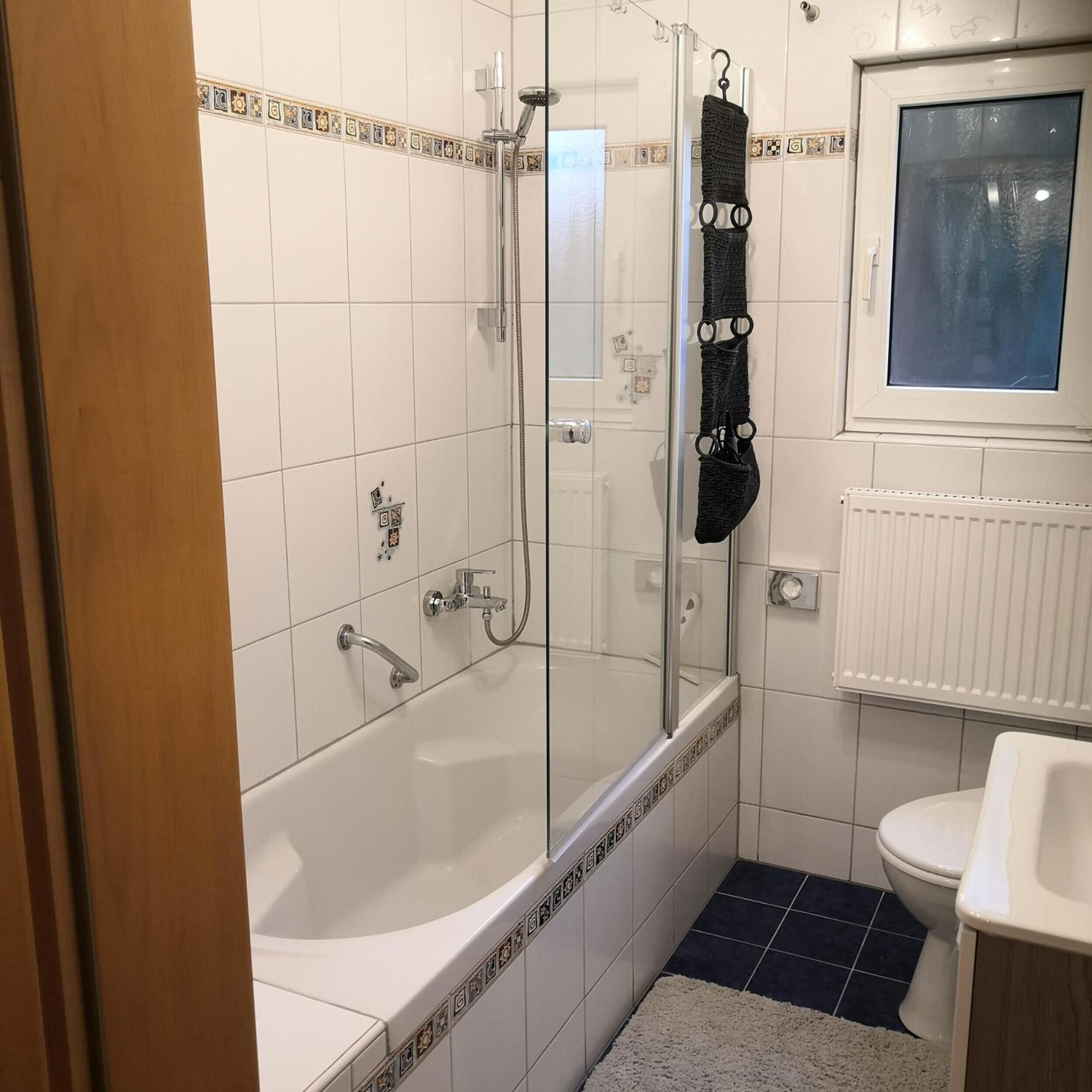 Un baño con ducha de vidrio, bañera blanca, inodoro y ventana sobre el lavamanos.