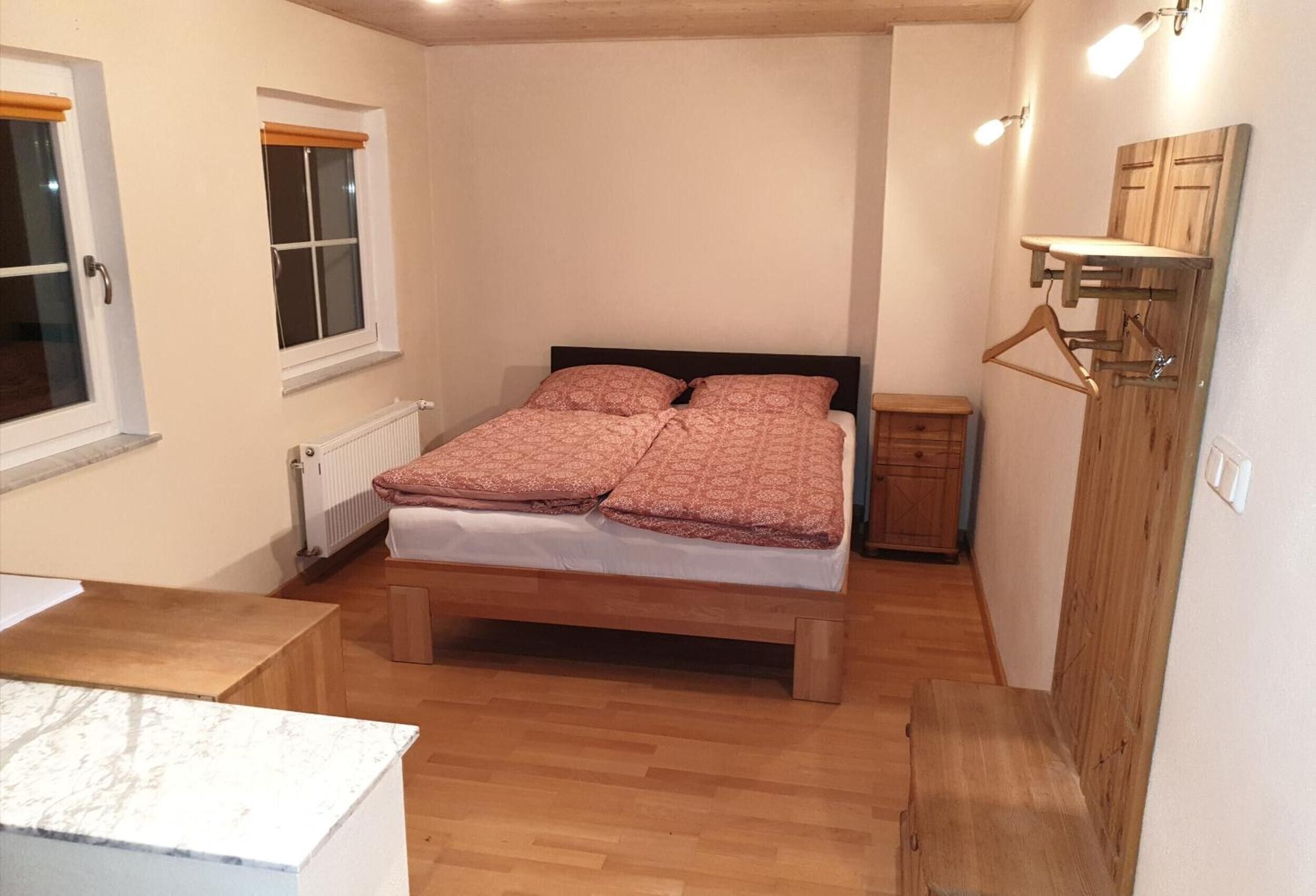 Ein Schlafzimmer mit einem hölzernen Bett, einem Nachttisch, einer Heizung, einem Holzschrank und einem Fenster mit Jalousien.