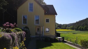 A yellow building with a porch, a car parked outside, and a green field in the background.