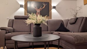 Un salon moderne avec un canapé d’angle, une table basse ronde et un tableau représentant un cerf, accroché au mur.