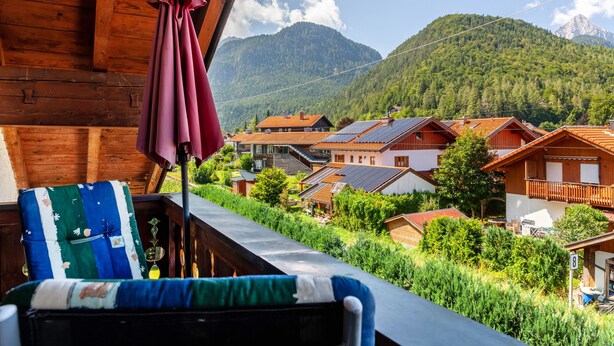 A balcony with a view of a mountain, wooden houses, and a chair with a blanket. - Apartment 'Wetterstein' with Mountain View, Balcony and Wi-Fi (Mittenwald)