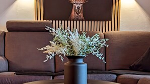 A round table with a vase of white flowers, a brown sofa, and a wall-mounted deer head decoration. - Apartment 'Wetterstein' with Mountain View, Balcony and Wi-Fi (Mittenwald)