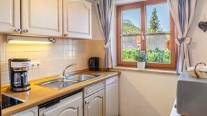A kitchen with a coffee maker, a kettle, a sink, and a window with curtains. - Apartment 'Wohnung 1' with Mountain View, Balcony and Wi-Fi (Mittenwald)