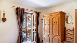 Un dormitorio con cama, armario de madera, silla y ventana con cortinas.