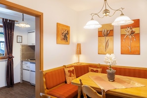 A dining area with a wooden table, orange upholstered benches, and wall-mounted artwork. - Apartment 'Wohnung 2' with Mountain View, Balcony and Wi-Fi (Mittenwald)