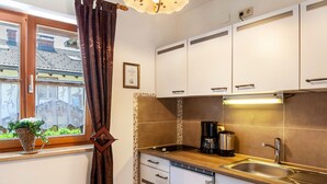 Una cocina con gabinetes blancos, un lavamanos de acero inoxidable, una cafetera y una ventana con vistas a casas.