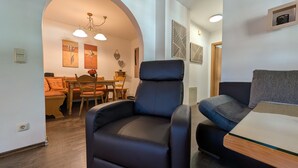 Una sala moderna con un sillón de cuero negro, un sofá, un comedor con mobiliario de madera y una araña.