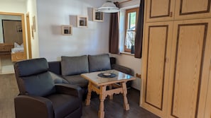 A room with a sofa, a small table, wooden cabinets, and a window with curtains. - Apartment 'Wohnung 2' with Mountain View, Balcony and Wi-Fi (Mittenwald)