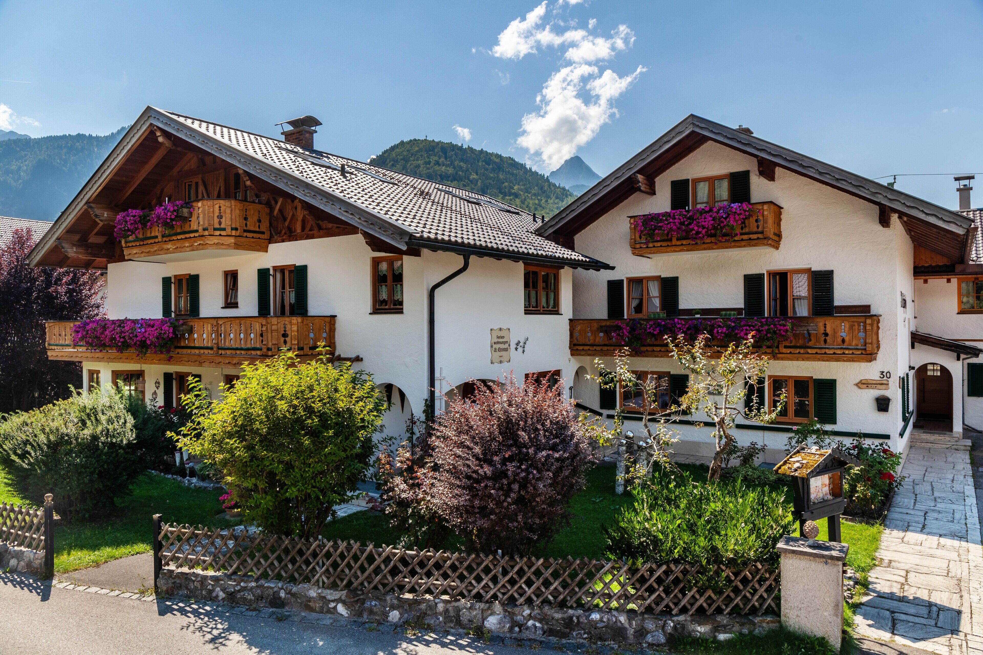 A traditional chalet with wooden balconies, a stone pathway, and a mountain backdrop.